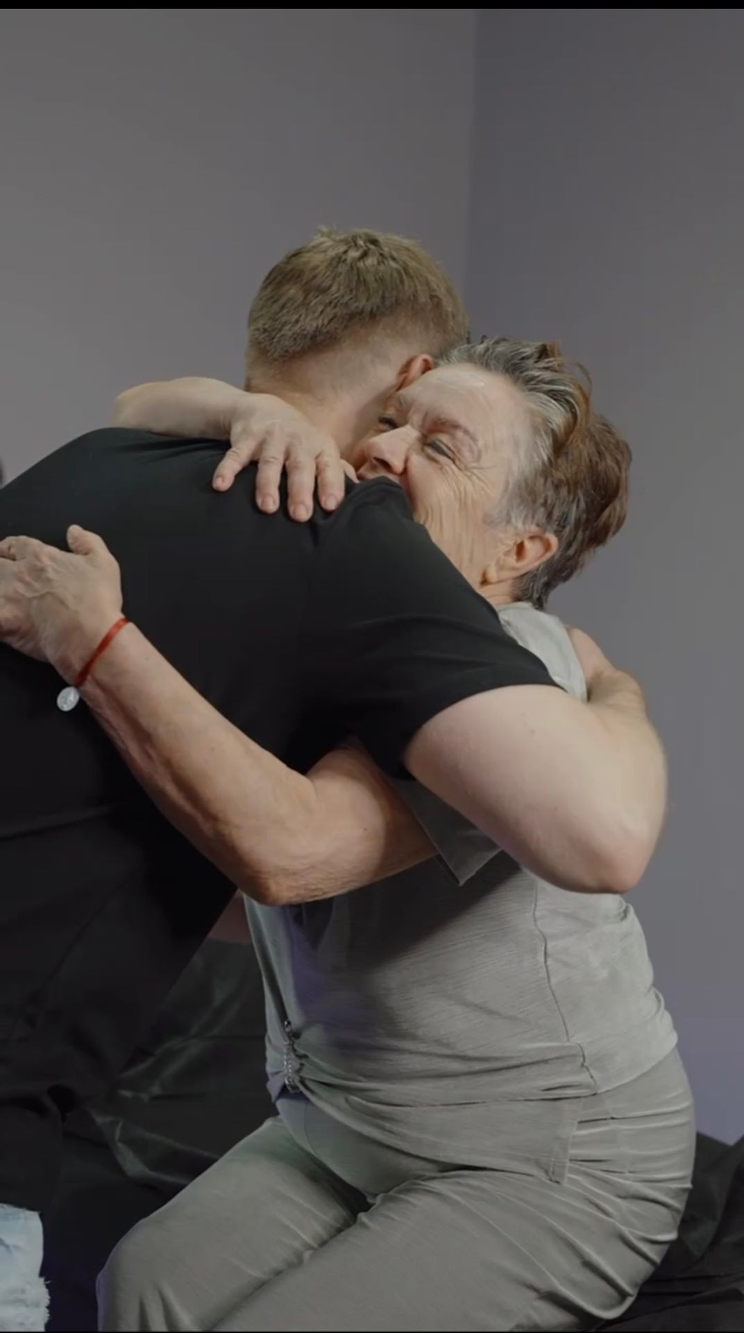 Elderly woman and young man hugging warmly in a room.